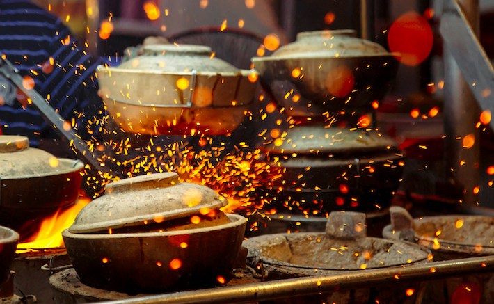 Covered pots cook on an industrial stovetop as flames pop around them