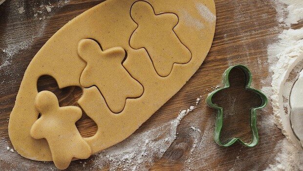 Cookie dough with three gingerbread-man shapes cut out of it