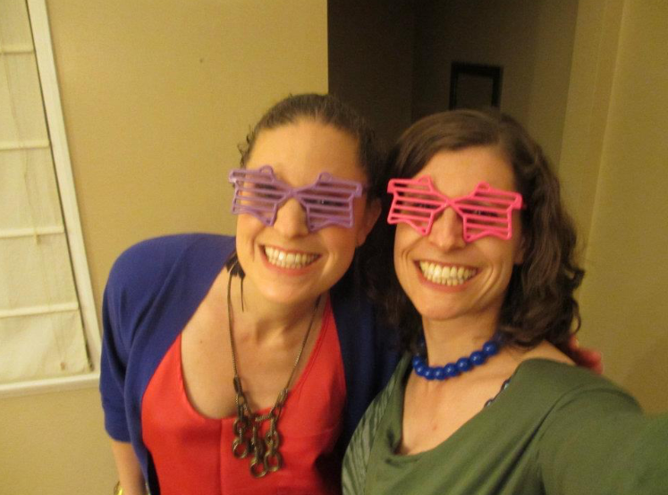 Sisters with light brown hair and star-shaped party glasses grin with their arms around each other