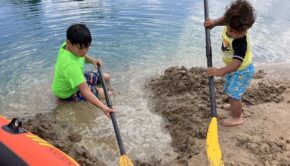 Two young boys dig in the sand with oars