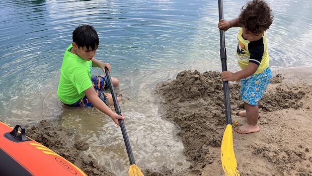 Two young boys dig in the sand with oars